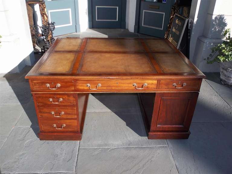 English mahogany leather top partner's desk with original brasses, each pedestal side identically fitted with three frieze drawers, three additional drawers and a cupboard door, all on a plinth base with original raised casters.  George III-style,