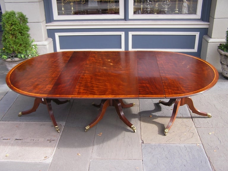 Irish plum pudding mahogany triple pedestal oval dining room table cross banded with Carpathian Burl Walnut and Satinwood. Pedestal has reeded legs ending on original brass claw casters. Table has two 10 5/8 
