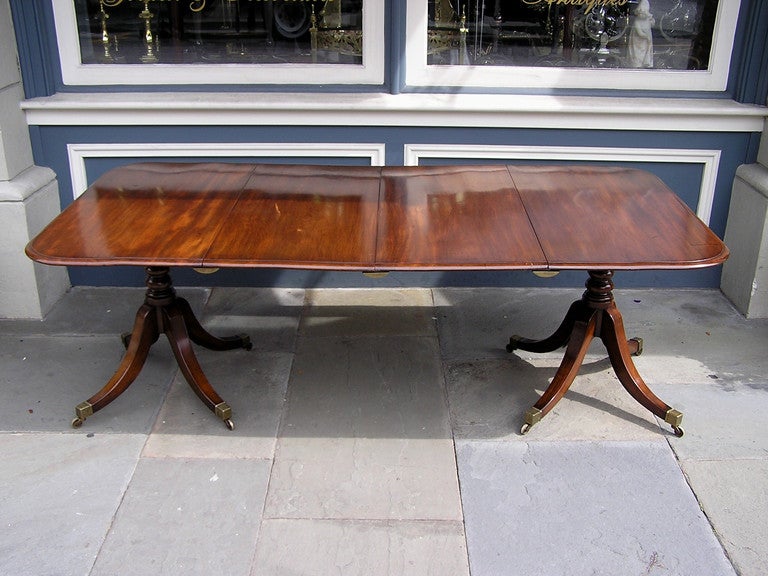 English mahogany two pedestal dining room table with removable  two leaves, turned and reeded pedestal, ending on original brass casters. Dealers please call for trade price.