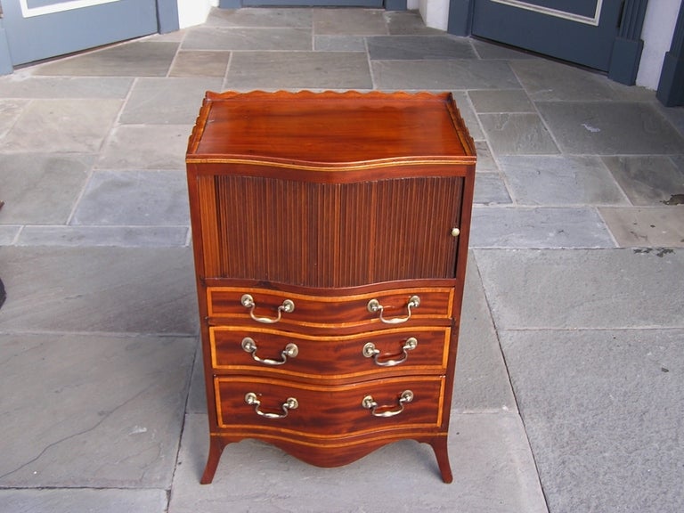 English mahogany graduated three drawer tambour top chest with carved molded gallery, rosewood inlay, original brass pulls and side handles, and terminating on carved serpentine skirt with splayed feet. All original. Dealers please call for trade