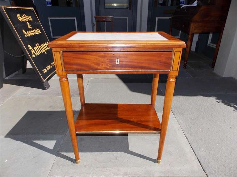 American Cherry marble top side table with one drawer pull out fitted interior desk, lower shelf,  brass banding, and terminating on brass cup feet. Baltimore, Circa 1810.