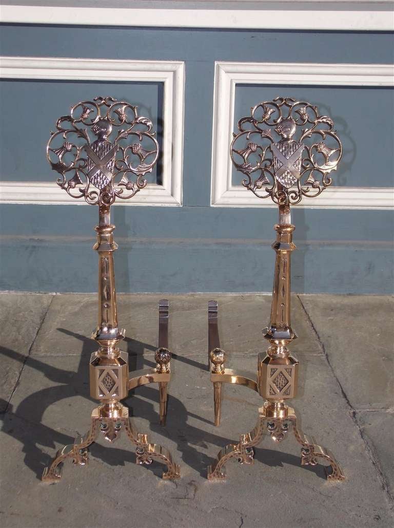 Pair of French polished bell brass medallion andirons with centered floral coat of arms, tapered hand chased faceted plinths, matching ball log stops, and terminating on scrolled hammered Fleur-de-lis legs. Early 19th Century