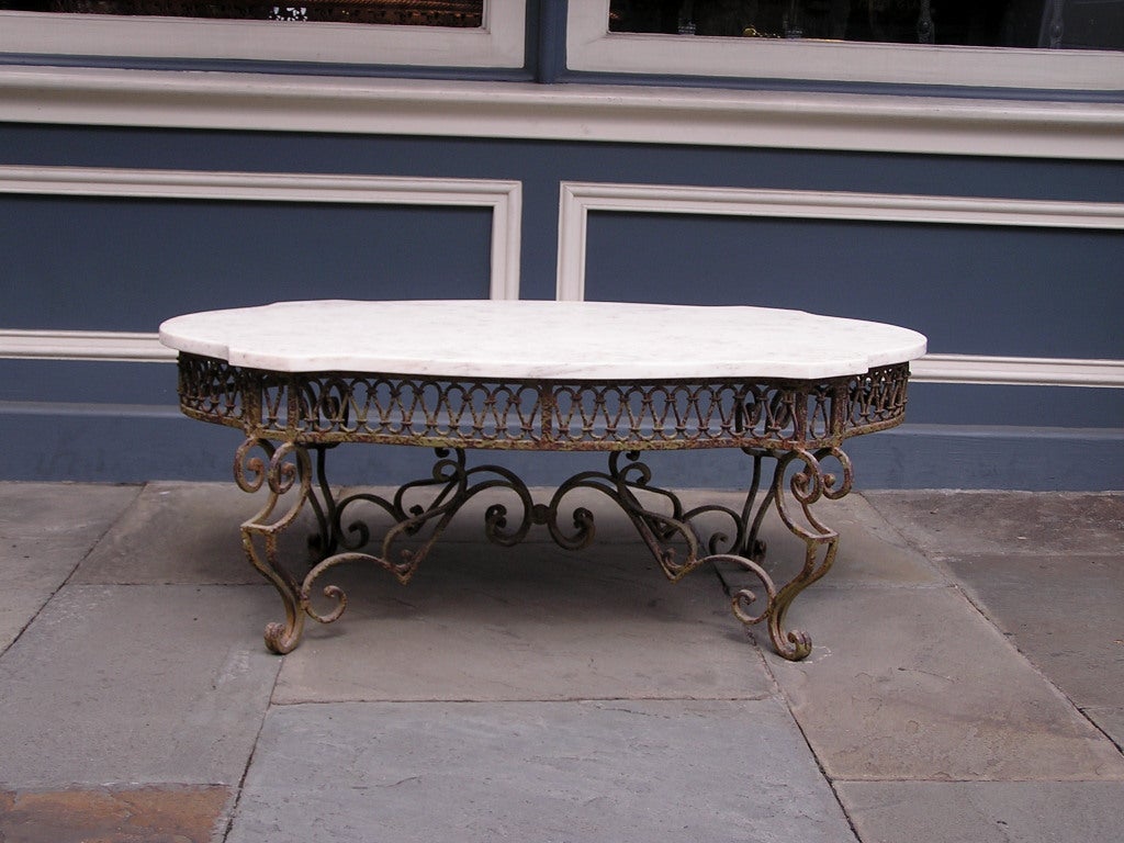 Tavolo francese in marmo e ferro battuto con intriquet a galleria intrecciata e terminante su gambe decorative a voluta.