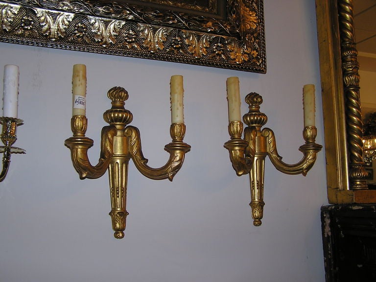 Pareja de apliques franceses de dos brazos de madera tallada y dorada con motivos florales y de urna. Originalmente velas. 