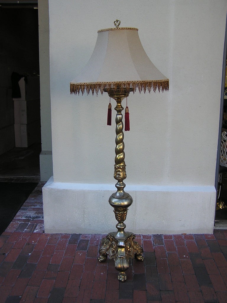 Lámpara de pie francesa de dos luces, de bronce dorado, con fuste retorcido con volutas, que conecta con la urna bulbosa floral inferior y termina en una base trípode de garras florales con figura decorativa.  Los vendedores pueden llamar para