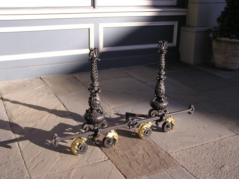 Pair of Italian Neoclassical wrought iron and brass foliage andirons with flanking decorative basket finials, central urn plinths, decorative adjustable cross bar with spit hooks, and resting on brass acanthus iron scrolled legs. Late 18th Century