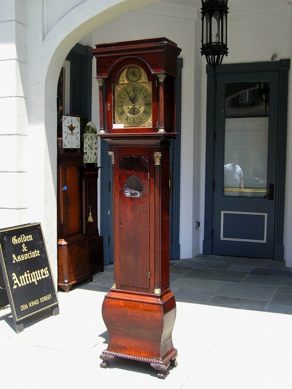 English mahogany tall case clock with dental molded rectangular hood supported by upper and lower gilt bronze Corinthian columns, dolphin ormolu face, carved shell trunk door, terminating on bombay shaped plinth with a carved molded edge on ball &