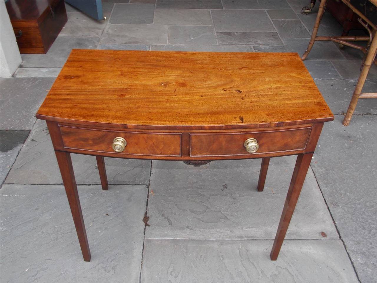 English bow front mahogany two drawer server with original brass pulls, one board top, and terminating on tapered squared legs.  Late 18th Century