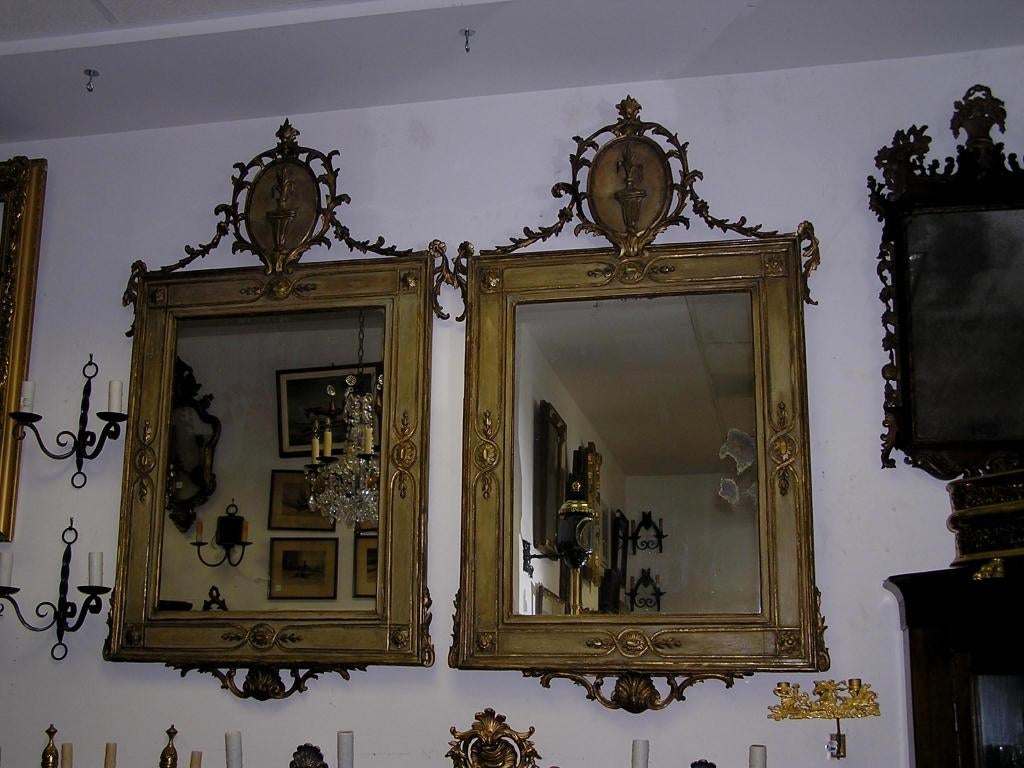 Pair of Italian gilt carved wood and painted wall mirrors with flanking centered oval floral crest's and intricately gilt carved foliate shell scrolls. Mirrors retain the original glass & wood backing. Late 18th Century