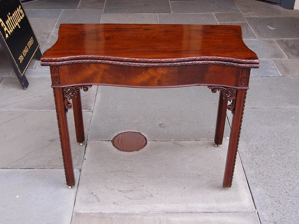 English Chippendale Cuban mahogany serpentine flip top game table with carved floral edge, corned fret work, and terminating on molded egg & dart legs with original barrel casters. Game table has a one board top. Circa 1760