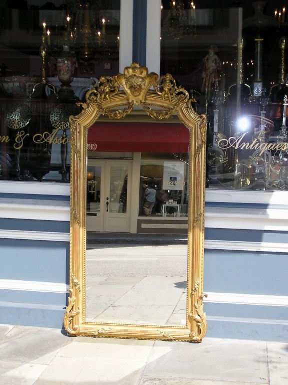 Miroir mural en bois doré et gesso avec médaillon de feuillage et crête de chérubin, avec perlage intérieur, bordure de ruban et motif d'acanthe en bas, début du 19e siècle. Le miroir a conservé son verre argenté d'origine.