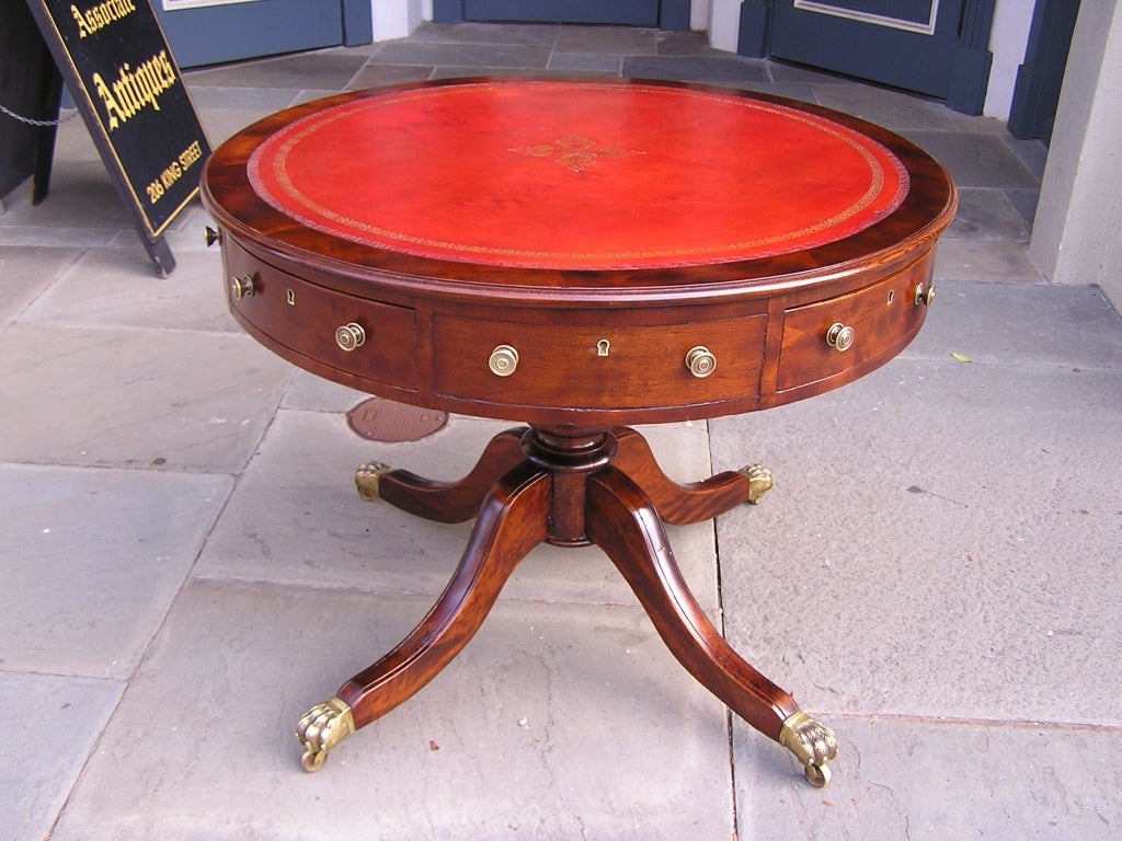 English mahogany four drawer rent table with rotating leather top, original brass knobs, and terminating on turned bulbous four leg pedestal with original lions paw casters.