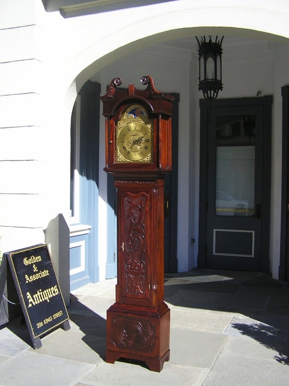 Irish Mahogany tall case clock with scrolled floral broken pediment, fluted hood columns, lunette moon phase, ormolu dial,  carved Celtic dragon trunk, carved floral base panel, and ending on original bracket feet. Clock is signed John Gelston,