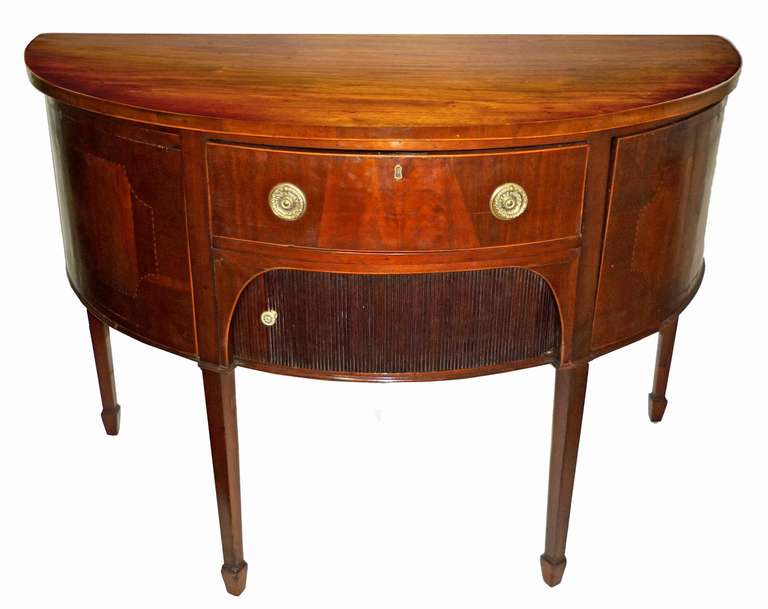 D Shaped top over a drawer and a tambour covered compartment; flanked with cabinets; raised on square tapering legs with spade feet.