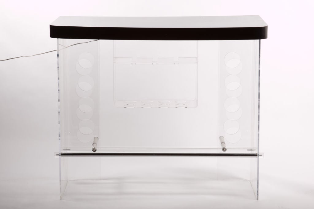 An illuminated bar of clear lucite with a sophisticated black top testifies to the stunning lucite wizardry of the 1970s.  The bar offers revealing storage for wine and liquor bottles as well as a roomy top for mixing and pouring.