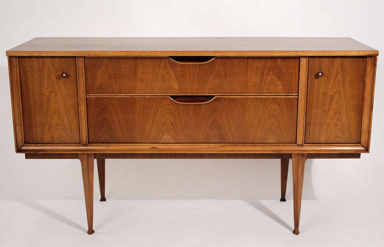 Modestly scaled credenza or sideboard cabinet with a thin profile on tall tapered and sculpted legs by Tomlinson. Finished back as pictured.