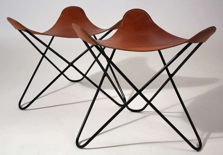 A pair of Jorge Hardoy for Knoll butterfly chair ottomans. Function great as a pair of stools. Each piece has full-grain, natural oiled leather sling tops with black painted steel bases and are fully restored. One measures slightly larger than the