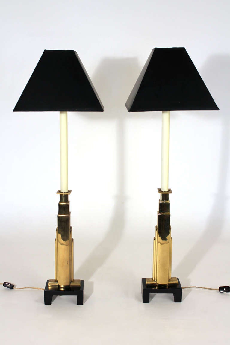 Pair of Chapman candle stick table lamps with brass finished columns on black lacquered wood bases. Original shades with black exteriors and gold colored interiors giving a warm ambiant light.

Shades measure 9