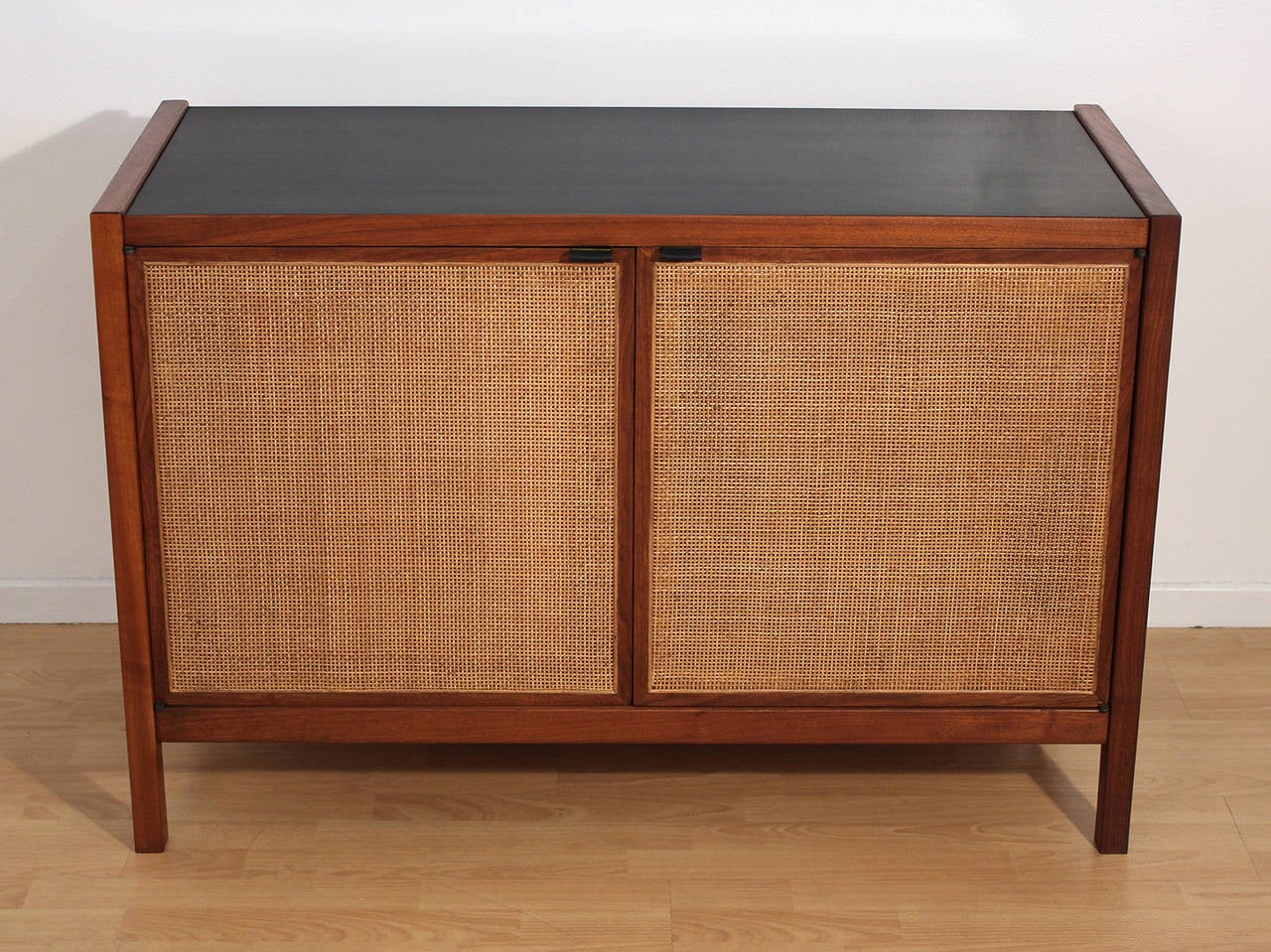 Small-scale credenza or cabinet made of solid walnut with cane doors, leather pulls and smooth black laminate top designed by Florence Knoll for Knoll Associates.

Excellent condition.