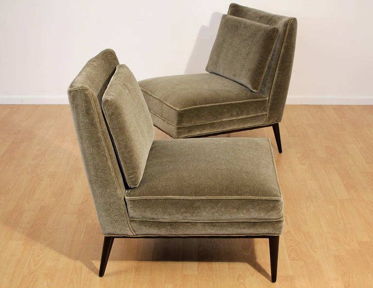 Pair of slipper lounge chairs with slightly curved wingback form and tapered legs designed by Paul McCobb. Upholstered in a soft pale olive green mohair velvet with loose cushions.