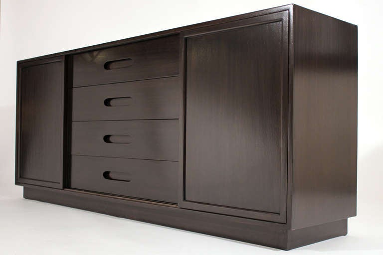 A four drawer credenza or chest of drawers with two sliding doors. Four white lacquered drawers on the left side and three while lacquered cork lined retractable shelves on the right. Designed by Harvey Probber. Dark brown lacquered finish.
