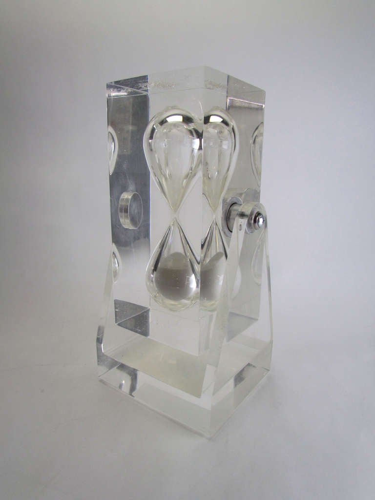 Massive Lucite hour glass consisting of a fine-grained two hour device embedded in a heavy block of clear acrylic suspended on a pivoting stand for ease of rotation, ca. 1960s.  

Measures 14.5