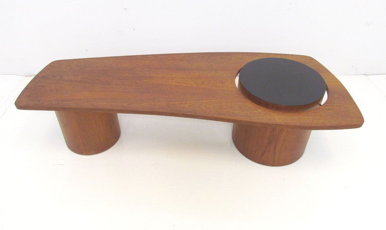 Mid-century modern teak coffee table with biomorphic asymmetrical top, supported by two teak cylinder pedestal bases, one of which is topped by a black laminate surface.    By R.S. Associates, Montreal. Canada, ca. mid-late 1960s. One of a series of