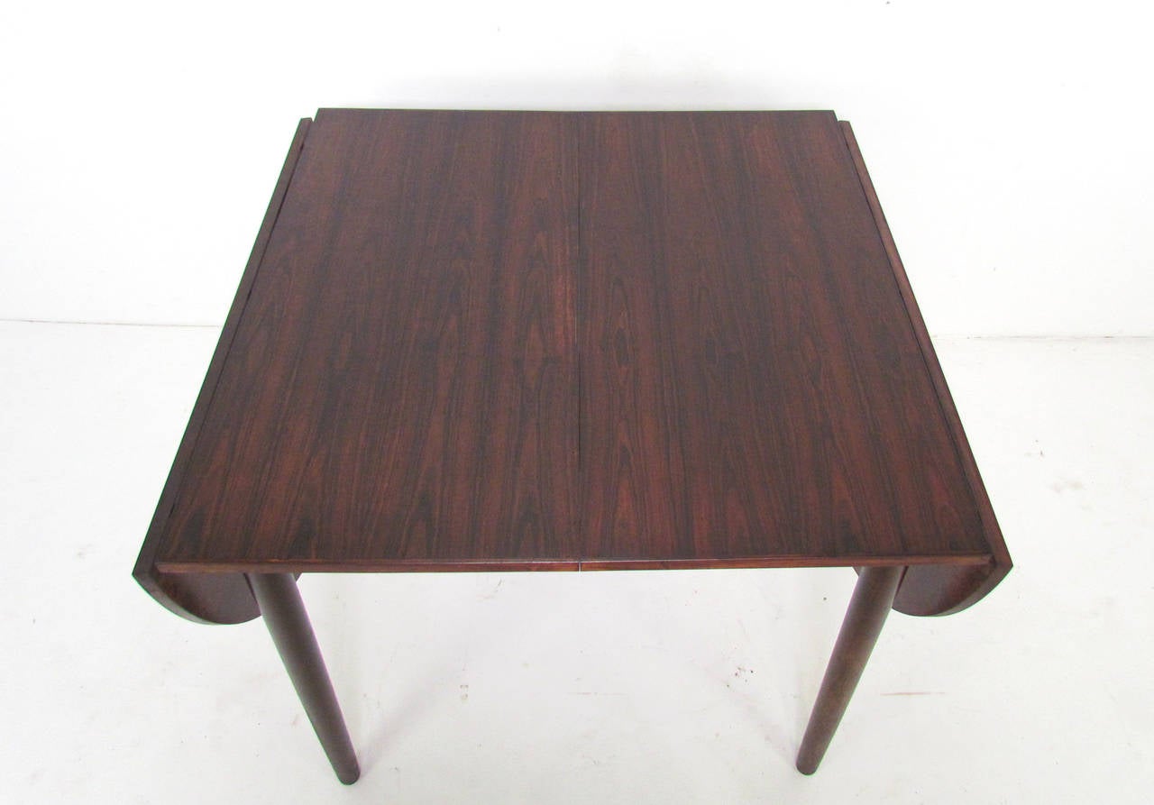 Versatile and expandable Danish dining table in rosewood with highly figured book matched leaves attributed to Arne Vodder for Sibast, circa 1960s. 

With the demilune drop leaves in the downward position, the table surface is 33
