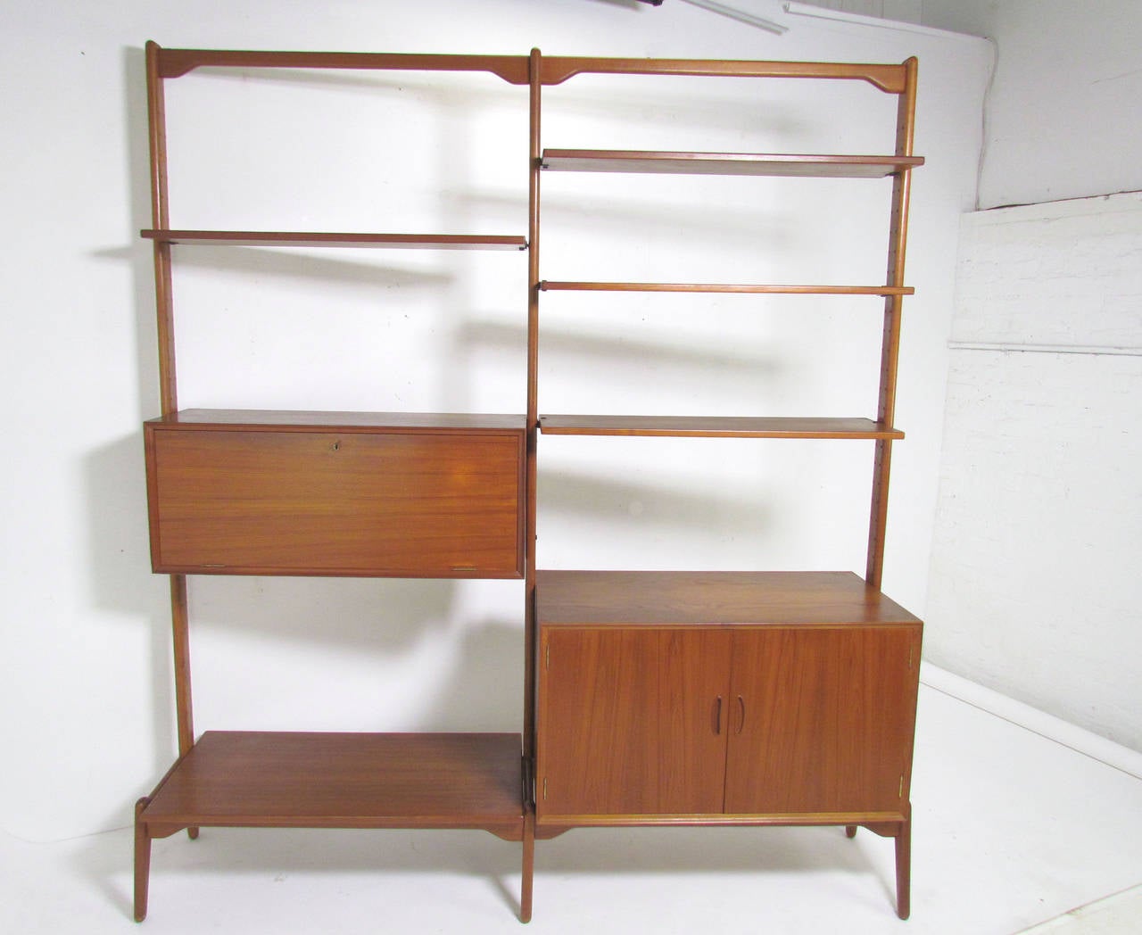 Danish teak freestanding wall unit attributed to Kurt Ostervig for Randers Mobelfabrik, circa 1960s. Large cabinet and deeper shelf at bottom level, with a bar or desk cabinet and remaining shelves which can be configured to your needs. 

Interior
