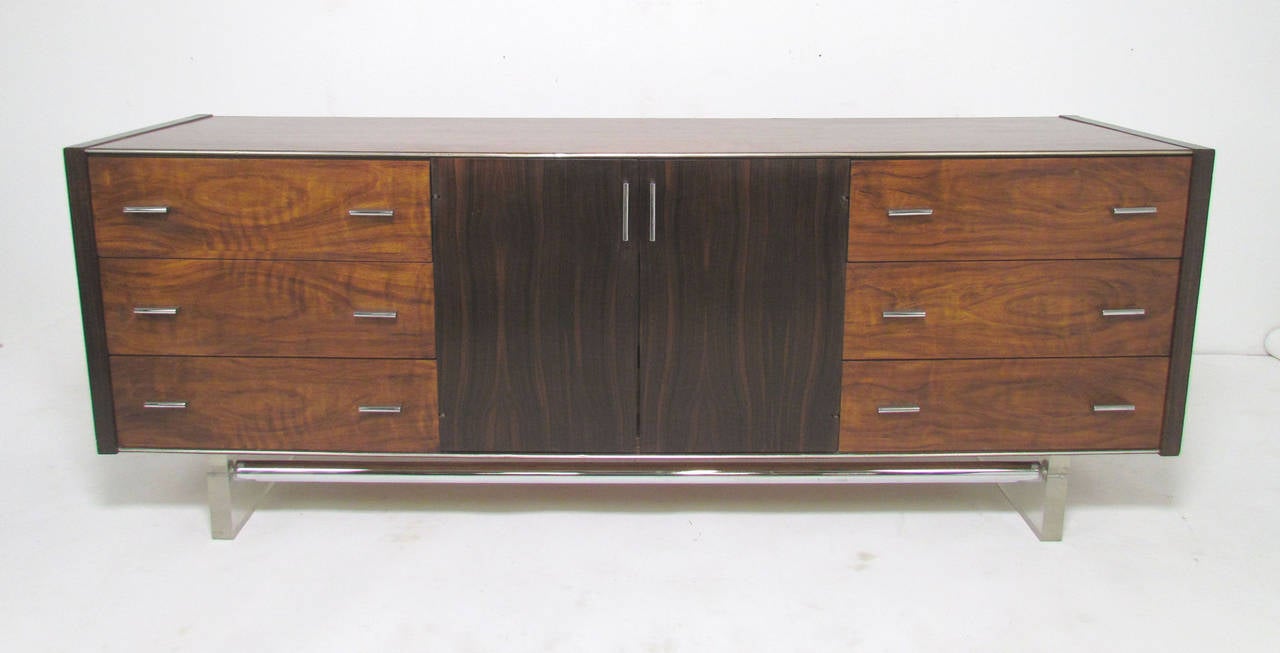 Mid-Century Modern long low credenza style nine-drawer dresser by Modernage Furniture Co. in rosewood and walnut with Lucite legs and chrome accents, circa 1960s, in the manner of Milo Baughman.

A matching pair of nightstands is also available.