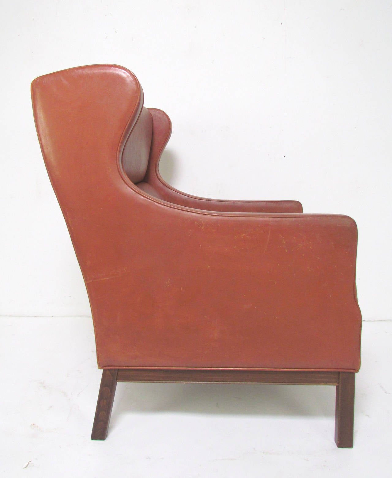 Danish wingback lounge armchair in original leather upholstery, in the manner of Børge Mogensen, circa 1950s. The original leather is distressed but still quite handsome. Rosewood legs and frame.