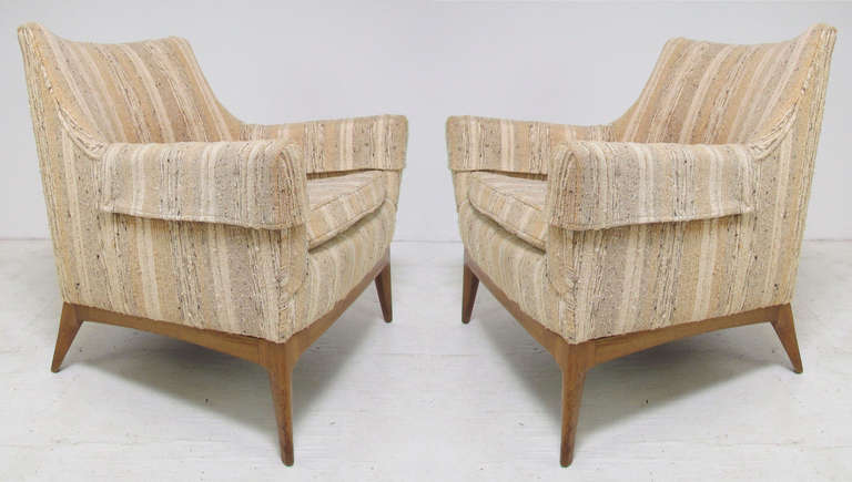 Pair of mid-century upholstered lounge arm chairs circa 1960s.  Elegant walnut bases and flared arms in the manner of Paul McCobb.