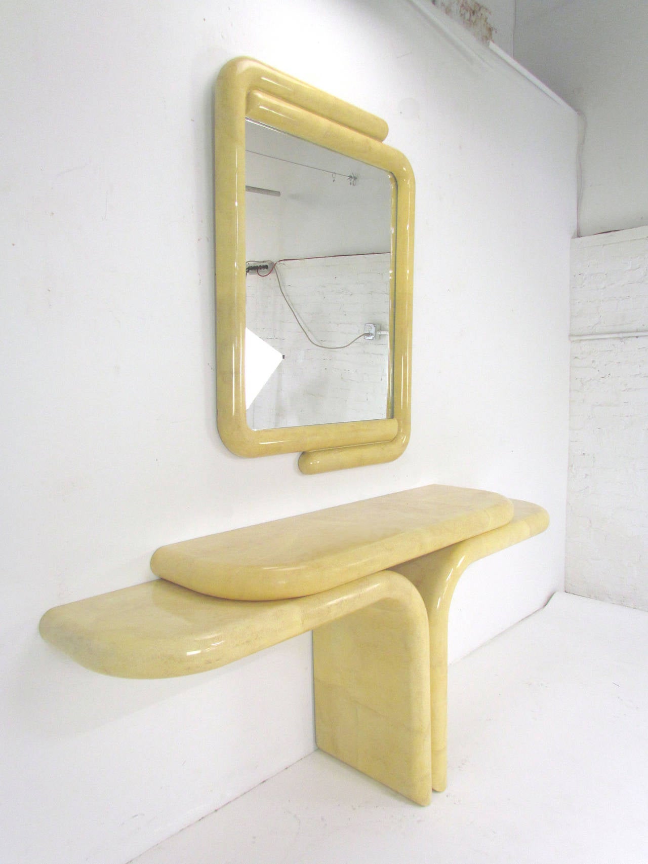 Sculptural console and mirror in the manner of Karl Springer. Lacquered in a faux goatskin finish, it features a counter balanced two-tiered table (with wall brackets for support) and a matching mirror that echoes its sinuous lines.
Mirror can be