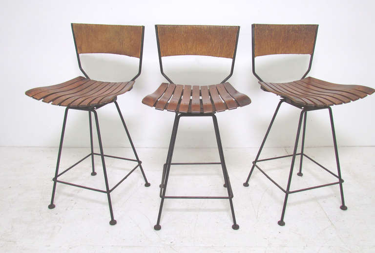 Set of three mid-century classic maple slat swivel bar stools with Danish cord backs and wrought iron frames designed by Arthur Umanoff for Raymor, ca. 1950s.  These are counter height stools, withseats 25