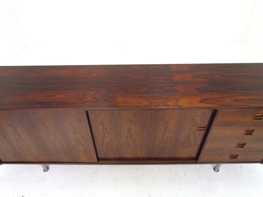 Sleek Danish rosewood long and low credenza with chrome legs, ca. 1970s.  Finished interior, single shelf behind sliding doors.  Four drawers on right.  Carved inset pulls.