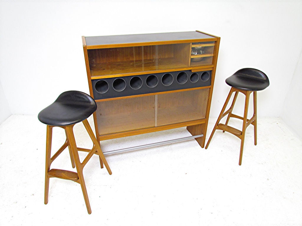 Danish teak dry bar and two stools, a collaboration between Erik Buck and Poul Heltborg that was marketed as a set in the Domus Danica catalog, ca. 1968.  Multiple compartments for storage of liquor bottles, pull out trays hold removable stainless