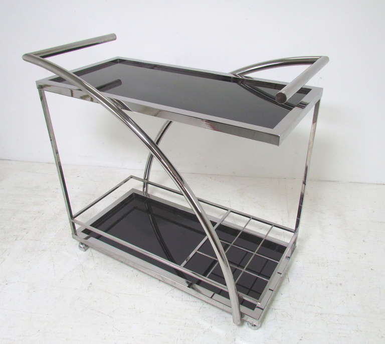 Sleek and stylish bar cart in chrome with black glass shelves in the manner of Milo Baughman.   Unusual sculptural curved handles, room for bottle storage and a rack for hanging stemware.