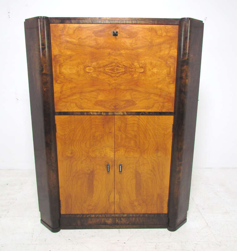 Art deco cocktail cabinet with panoramic book matched burl wood doors set against contrasting dark stained birch.  Drop down service bar with mirror back and glass shelf for drinkware, and flanking backlit panels.   Under cabinet with ample height