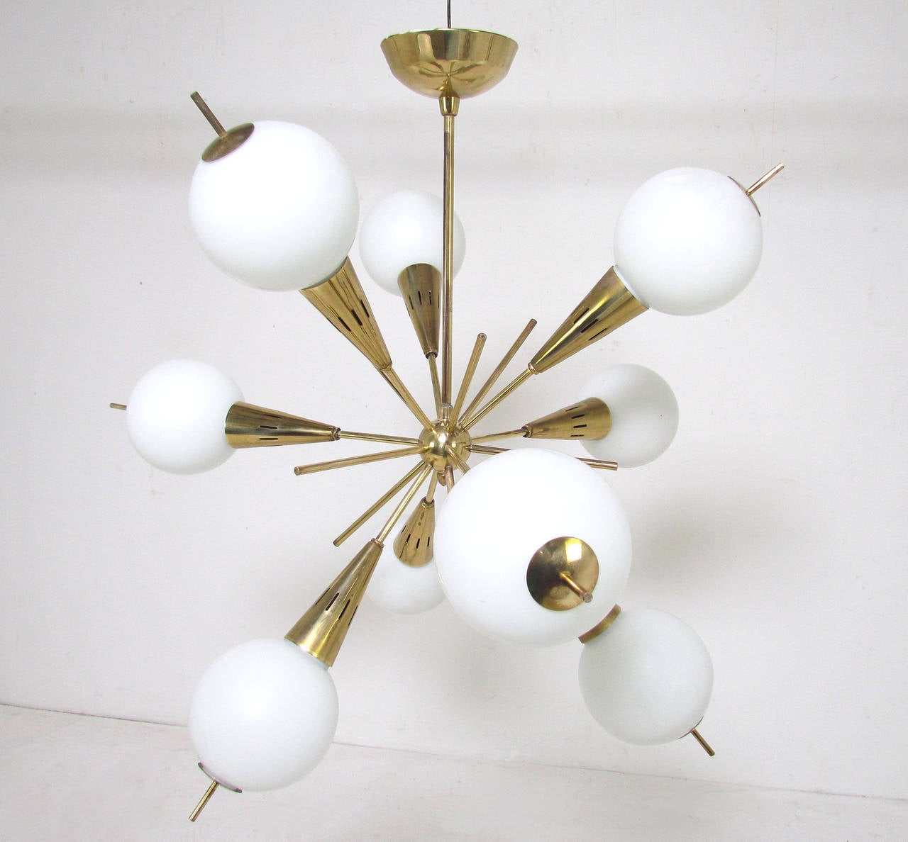 Rare form mid-century modern chandelier, circa 1960s with unusual pierced globes, a form often attributed to Stilnovo. Nine cone shaped brass arms with illuminated glass globes and brass end caps, and emanating decorative brass rods.