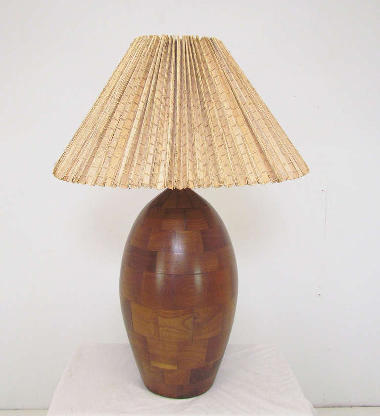 Magnificent hand made studio table lamp in a patchwork of staved walnut blocks.  Sensual ovoid form with original palm leaf shade, ca. 1960s.

32.5