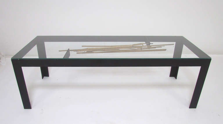 Brutalist coffee table with lacquered steel legs and glass top over a suspended wire-work sculptural construction.  In a striking departure from 