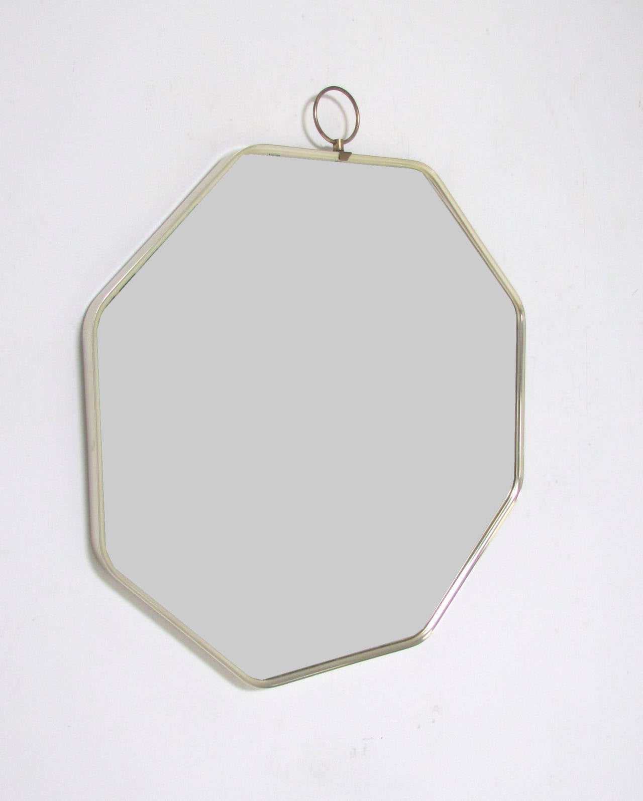 Italian modernist octagonal wall mirror with decorative top brass ring, circa 1960s, in the manner of Gio Ponti. Frame is anodized aluminum with a brass finish.