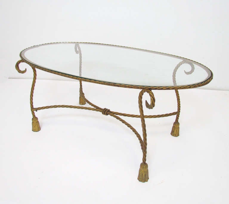 Hollywood Regency style gilt metal coffee table, rope-braided, scroll form base with inset oval glass top.  Retains its original stamped metal 