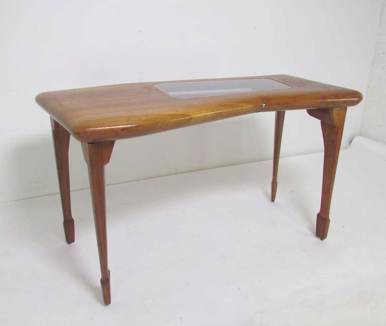 Unique studio craft made desk in walnut, circa 1950s,  with unusual central bijouterie element.  Asymmetrical stack laminated and carved top features a velvet lined and lighted display case for wares with a hinged bottom for access to contents. 