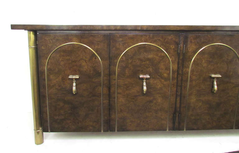 Hollywood Regency style sideboard designed by William Doezema for  Mastercraft, distributed by Charak Furniture, circa 1960s.  This credenza features amboyna and medium dark elm burl with solid brass pulls, arched brass door banding, and bronzed