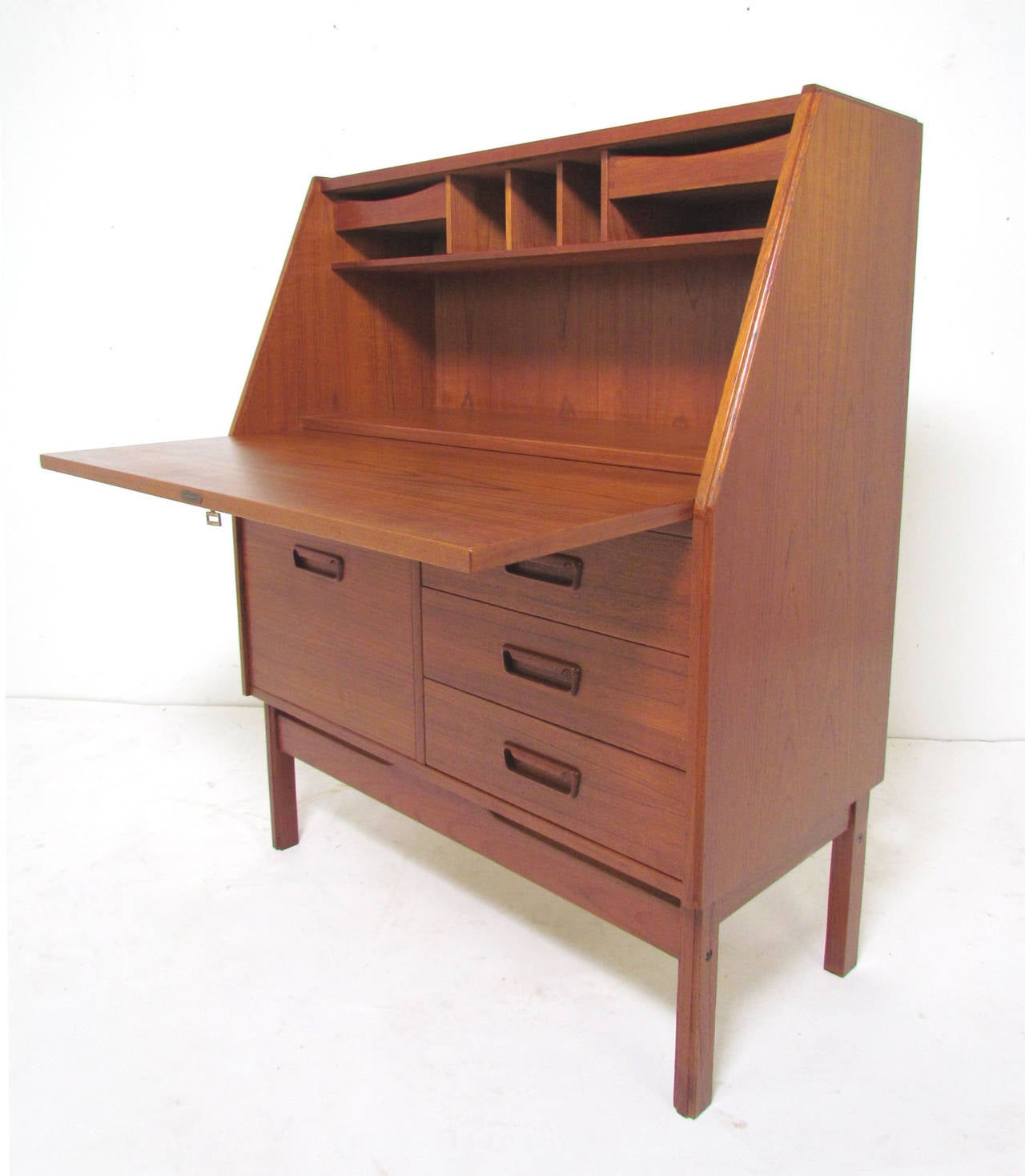 Low slant front teak secretary desk by Dyrlund, made in Denmark, circa 1960s. Interior features shelving and shallow drawers for storage. Below the desk surface there are four drawers including one deeper one for files.

Measures: 16.5