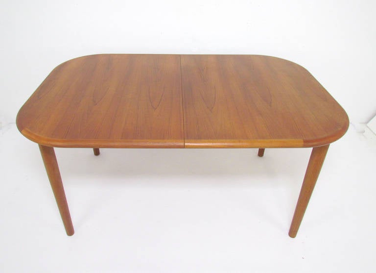 Danish teak mid-century modern dining table, with self-storing bookmatched butterfly extension leaf.  The leaf is affixed to the interior glides, for easy access and use.  

Measures 57.5