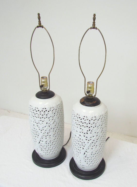 Pair of Blanc De Chine porcelain table lamps with cutwork decoration, ca. 1950s.  Ebonized wood accents at bases and caps.  Illuminated internally as well.  Remnants of original foil labels remain.  19