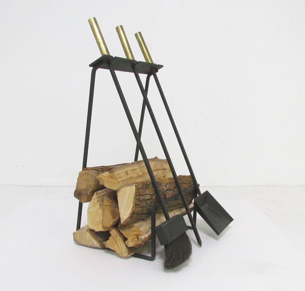 Mid-Century Modern fireplace tool rack with ingenious built-in log holder in wrought iron, with cylindrical brass wrapped handles, circa 1960s, in the manner of George Nelson.