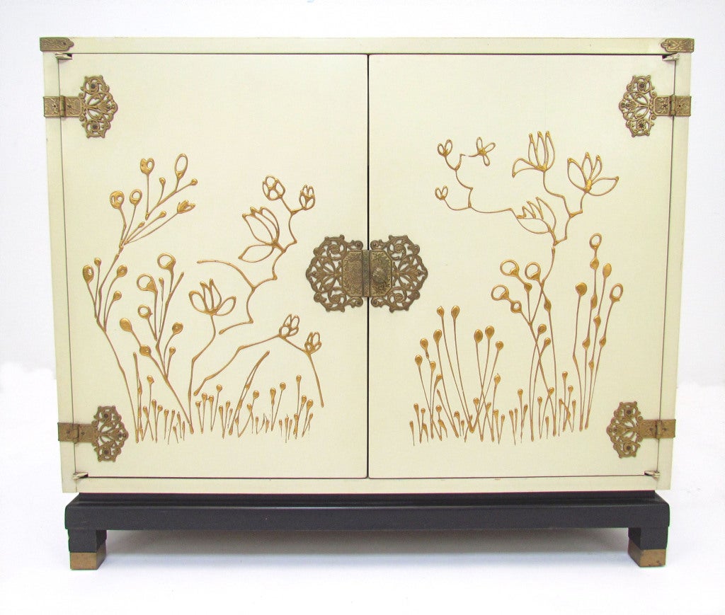Decorative cabinet with hand painted decoration, gilded top, elaborate brass hardware, and feet with brass sabots.  In the manner of Renzo Rutili for Johnson Furniture.
